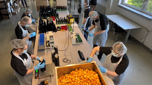 Mehrere Mitarbeitende mit Schutzkleidung füllen in einer Werkstatt große Mengen Popcorns ab.