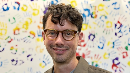 Schulleiter Marcus Kortmann steht vo einer Wand mit bunten Handabdrücken