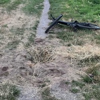 Auf einem Feldweg ist eine Mulde mit Stroh und Gras verdeckt, dahinter liegt ein Fahrrad auf dem Boden