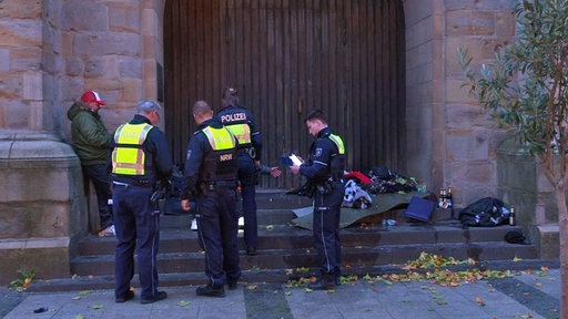 Polizisten vor  dem Portal einer Kirche mit Kleidung von Obdachlosen