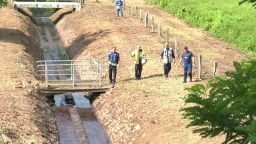 Feuerwehrleute gehen auf dem Ruhrdeich den trocken gelegten Zufluss zur Ruhr ab