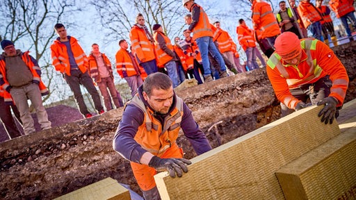 Die Bauarbeiter setzen die Steinwolle in die Grube an der Baustelle in der Alleestraße