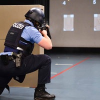 Eine Person mit Helm und Weste der Polizei, kniet vor zwei Karton und zielt mit einer Waffe auf Ziele