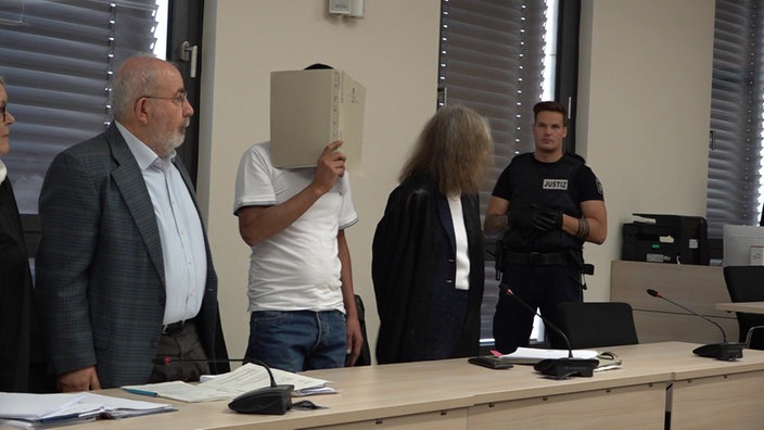 Der Angeklagte im Gericht verdeckt sein Gesicht mit einer Akte