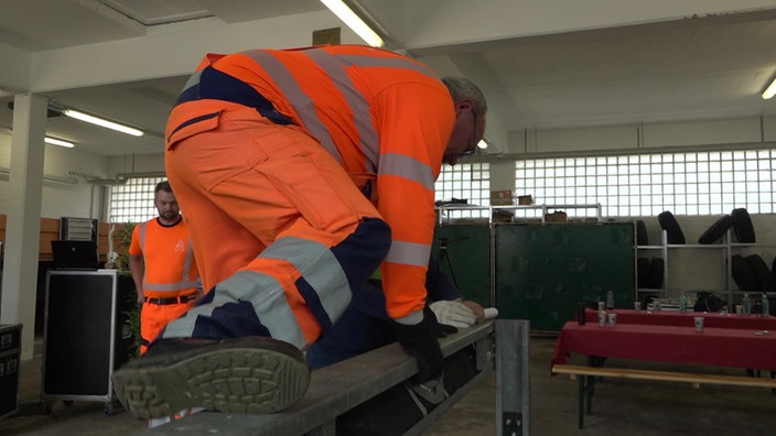 Person in Orangenen Arbeitsklamotten klettert über eine LKW Leitplanke