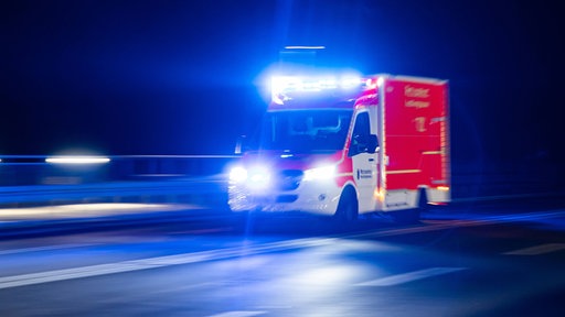 Auf dem Foto ist ein Rettungswagen, der nachts über eine Straße fährt.
