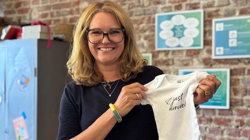 Personalchefin Kiki Radicke lächelt in die Kamera und hält einen Babybody in den Händen.