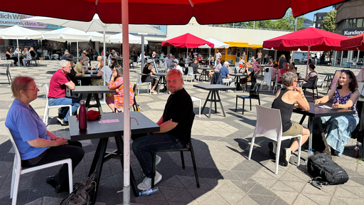 Im Vordergrund sitzen sich eine Frau und ein Mann gegenüber, um Sie herum sitzen noch mehr zweier Gruppen an Tischen 