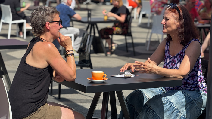 Zwei Frauen sitzen sich gegenüber, zwischen Ihnen steht eine Tasse und Sie Unterhalten sich