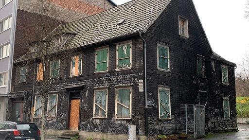 Ein verwahrlostes schwarzes Haus mit grünen, fleckigen Fensterläden.