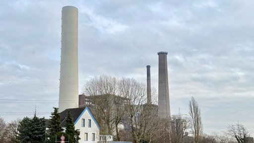 Drei Kraftwerkstürme ragen in den bewölkten Himmel. Davor ein Ausflugslokal und eine Straße.
