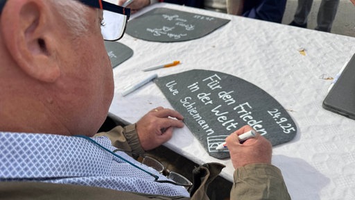 Ein Mann schreibt mit weißem Stift auf eine Schieferplatte "Für den Frieden in der Welt - Uwe Schiemann"