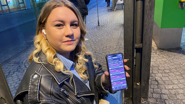 Ein Frau sitzt an einer Haltestelle und hält ihr Handy in der Hand.