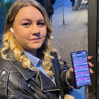 Ein Frau sitzt an einer Haltestelle und hält ihr Handy in der Hand.