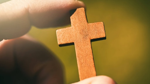 Ein Mann hält ein kleines Holzkreuz zwischen seinen Händen