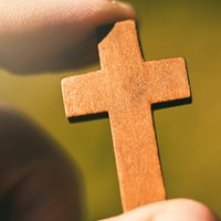 Ein Mann hält ein kleines Holzkreuz zwischen seinen Händen