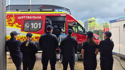 Gruppe vor rotem Krankentransporter, Leitstand