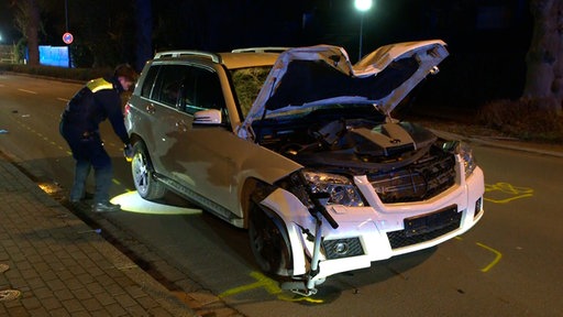 Ein beschädigter SUV mit offener Motorhaube, vorne klemmt ein E-Roller unter dem Fahrzeug