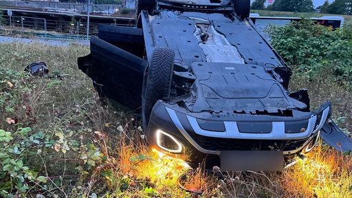 Das Bild zeigt ein Auto auf dem Dach nahe des Flussufers liegend.