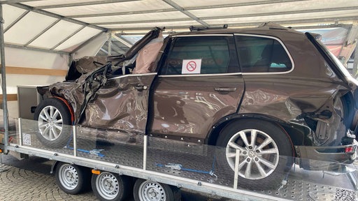 Ein Autowrack welches Vorne eingedrückt ist , steht auf einer Art Podest in einem Zelt
