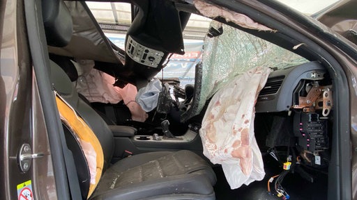 Innenanasicht eines Autowracks. Ein augelöster Airbag mit Blutspritzern und eine zebrochene Frontscheibe sind zu erkennen