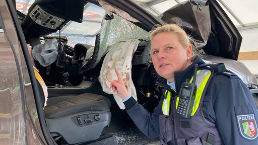 Polizistin Melanie Bierr steht vor einem Autowrack und zeigt auf Blutflecken im Airbag 
