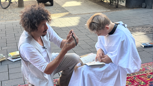 Danny Beuerbach kniet vor einem vorlesenden Jungen und schneidet ihm die Haare.