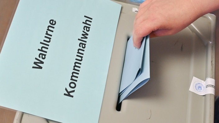 Ein roter und ein gelber Wahlzettel und ein Stift liegen auf einem Holztisch