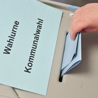 Ein roter und ein gelber Wahlzettel und ein Stift liegen auf einem Holztisch