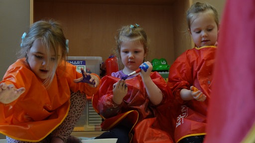 Leonie, Leni und Louisa bemalen sich ihre Hände mit Farbe und stempeln damit ihr Poster zu den Kinderrechten ab.