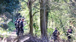 Mehrere Polizisten stehen in einem Wald.