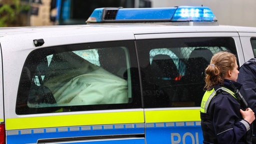 Eine Polizistin steht vor einem Polizeiauto, das Blaulicht an hat