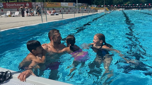 Ein Mann planscht mit drei Kindern in einem Freibadbecken