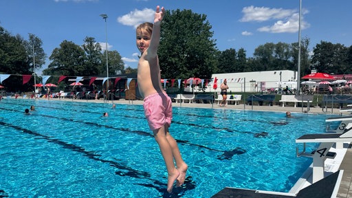 Eine Junge sprigt in ein Freibadbecken