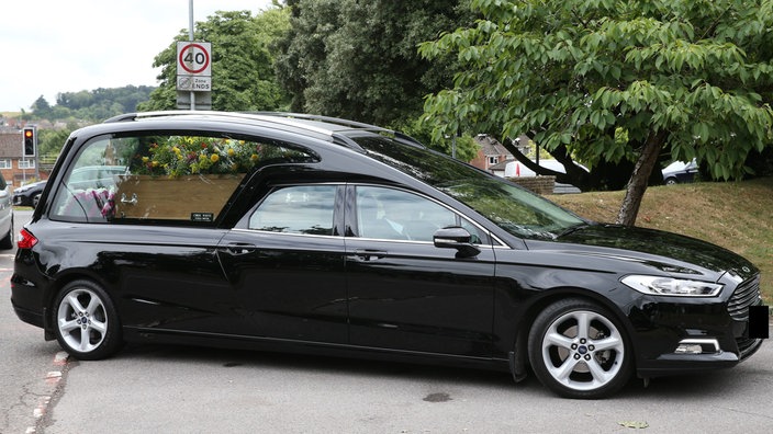 Ein schwarzer Leichenwagen auf einer Straße.