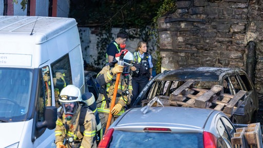 Die Feuerwehr steht neben einem abgebrannten Auto 