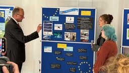 Bundeskanzler Friedrich Merz lässt sich eines der drei EU-Projekte von den Schülern erklären 