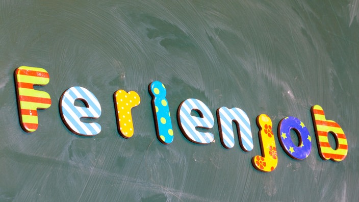 An einer Schultafel steht in bunten Buchstaben das Wort "Ferienjob".