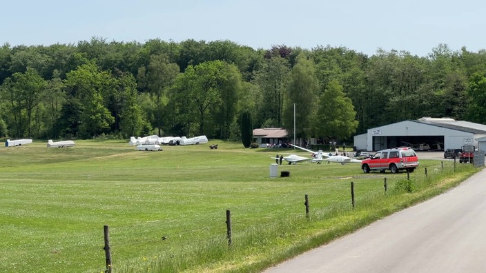 Der Flugplatz Hünsborn von Weitem. Einige Segelflugzeuge stehen auf einer Wiese vor einer Halle