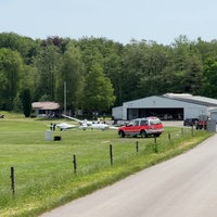 Der Flugplatz Hünsborn von Weitem. Einige Segelflugzeuge stehen auf einer Wiese vor einer Halle