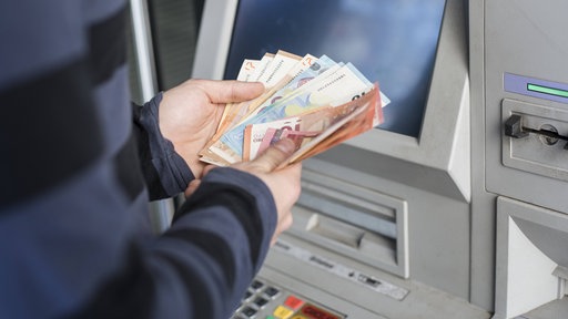 Eine Person hält mehrere Geldscheine in der Hand, die zuvor in einem manipulierten Automaten stecken geblieben sind.
