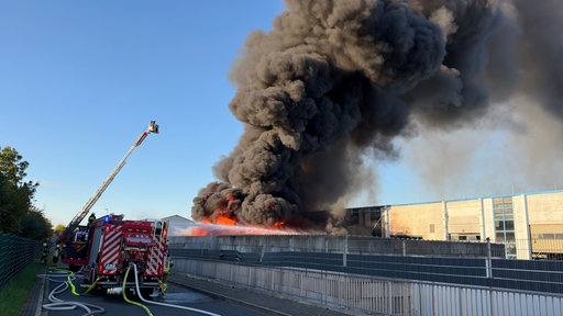 Ein Feuerwehrauto löscht einen großen Brand auf einem Firmengelände