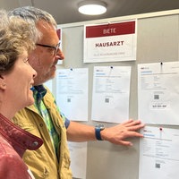 Ein Mann und eine Frau schauen auf eine Wand mit Inseraten