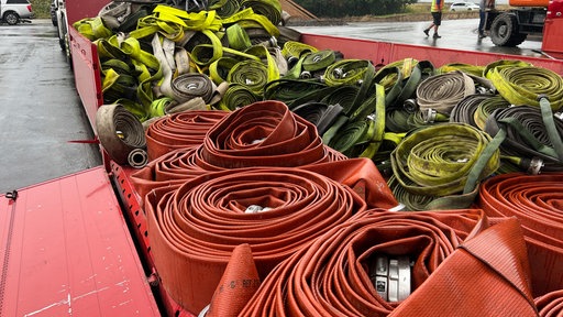 Große Menge aufgerollter Feuerwehrschläuche auf einem roten Anhänger.