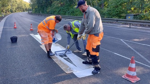 Bauarbeiter, die Pfeile auf den Asphalt streichen.