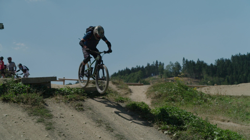 Ein Mountainbiker mit Helm und Schutzkleidung springt über eine Rampe