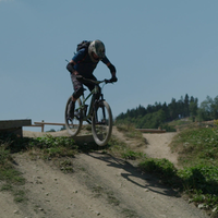 Ein Mountainbiker mit Helm und Schutzkleidung springt über eine Rampe