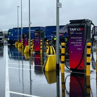 Mehrere Ladestationen für E-LKW auf einem Parkplatz. LKWs und Autos sind im Hintergrund.