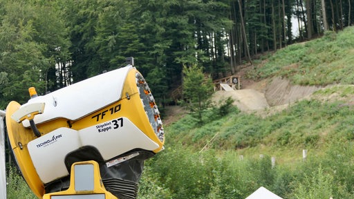 Eine Schneekanone im Vordergrund - Mountainbikestrecken im Hintergrund