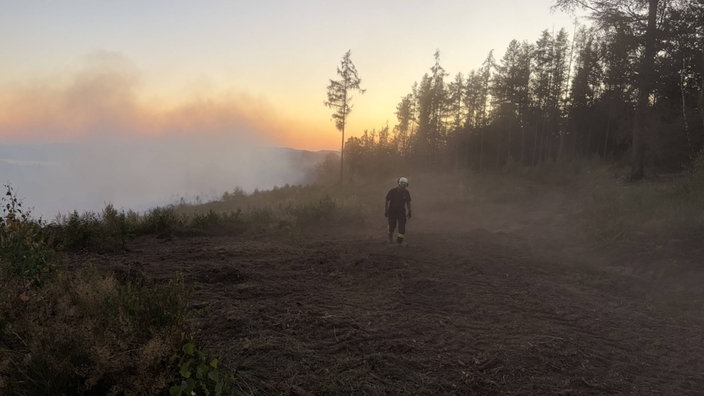 Ein Feuerwehrmann steht bei Sonnenuntergang im Rauch 